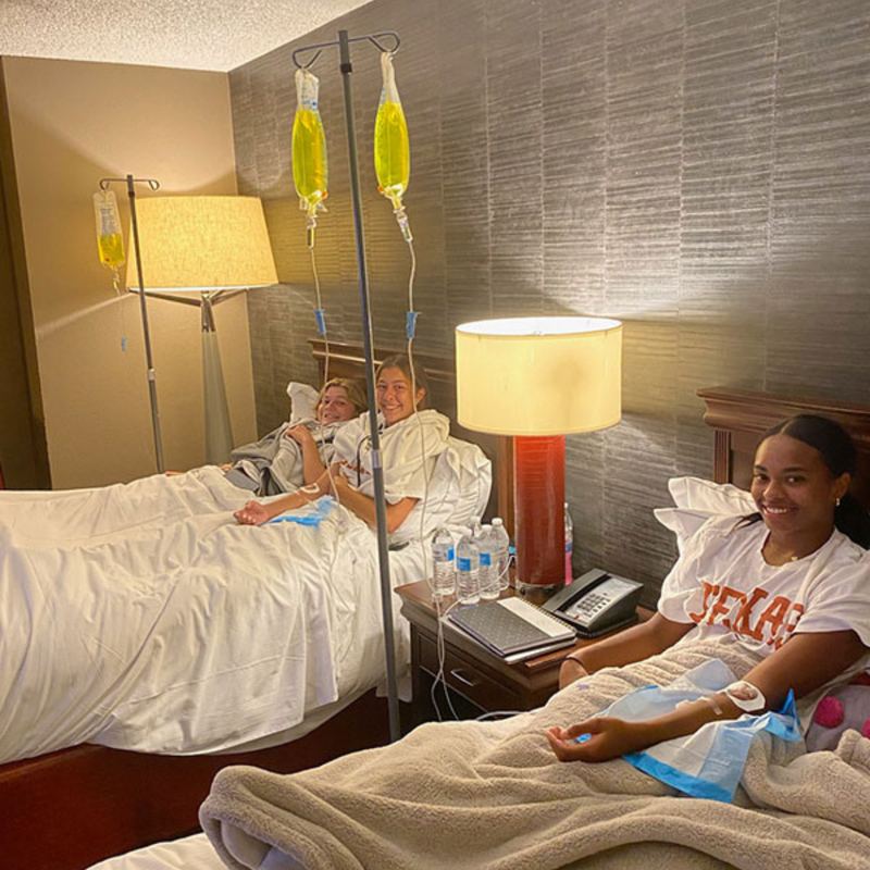 Three athletes resting on IV drips in a hotel room