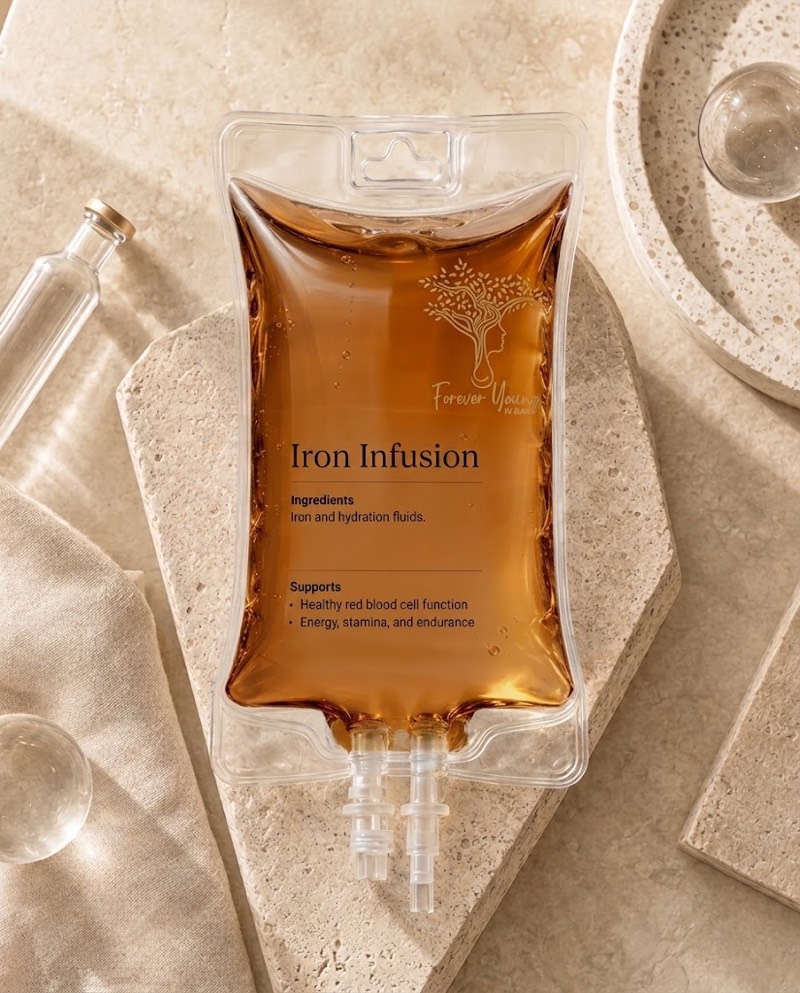 IV bag of amber iron solution labeled “Iron Infusion”, with the Forever Young IV Bar logo, on a cream stone tray